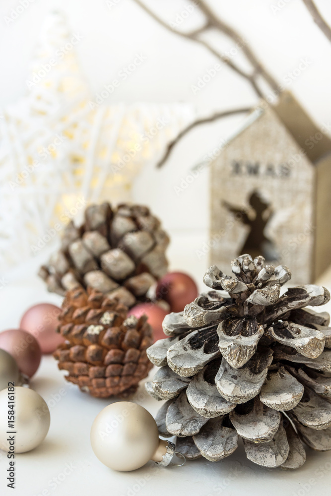White Christmas decoration composition, big pine cones, scattered baubles, shiny star, wooden candle holder, dry tree branches in background, minimalist