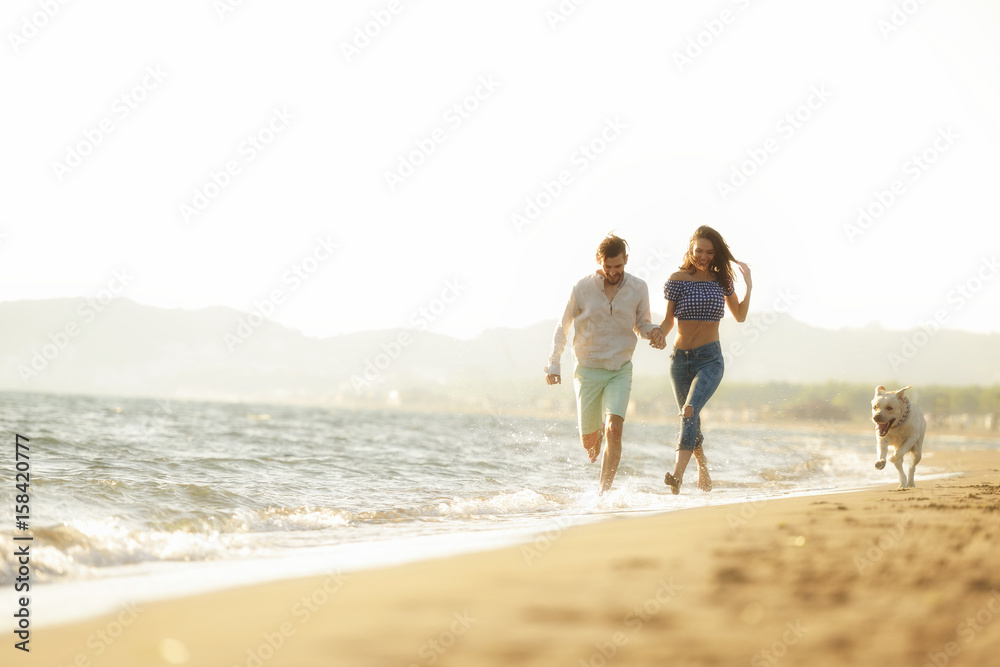 two young people running on the beach kissing and holding tight with dog