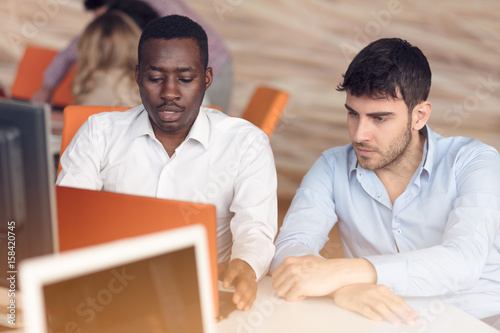 Image of two young businessmen interacting at meeting in office