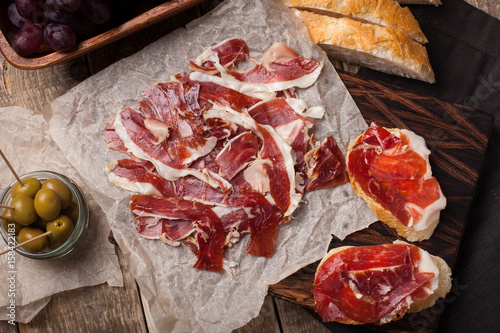 Jamon Iberico with white bread, olives on toothpicks and fruit on a wooden background. Top view photo