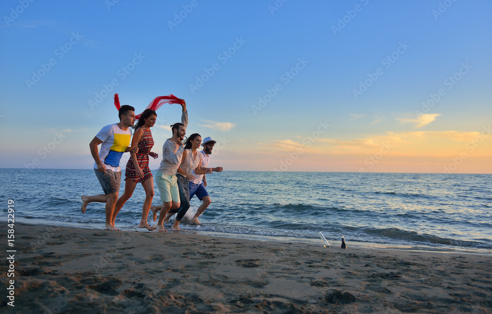 Group of happy young people is running on background of sunset beach and sea Group of happy young people is running on background of sunset beach and sea
