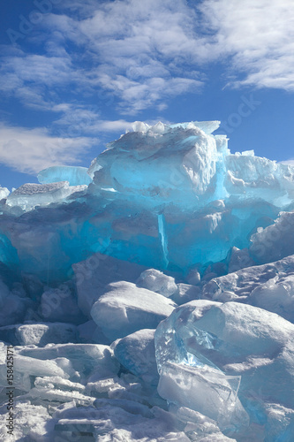 Hummocks of turquoise blue ice blocks covered with snow under white clouds, vertical