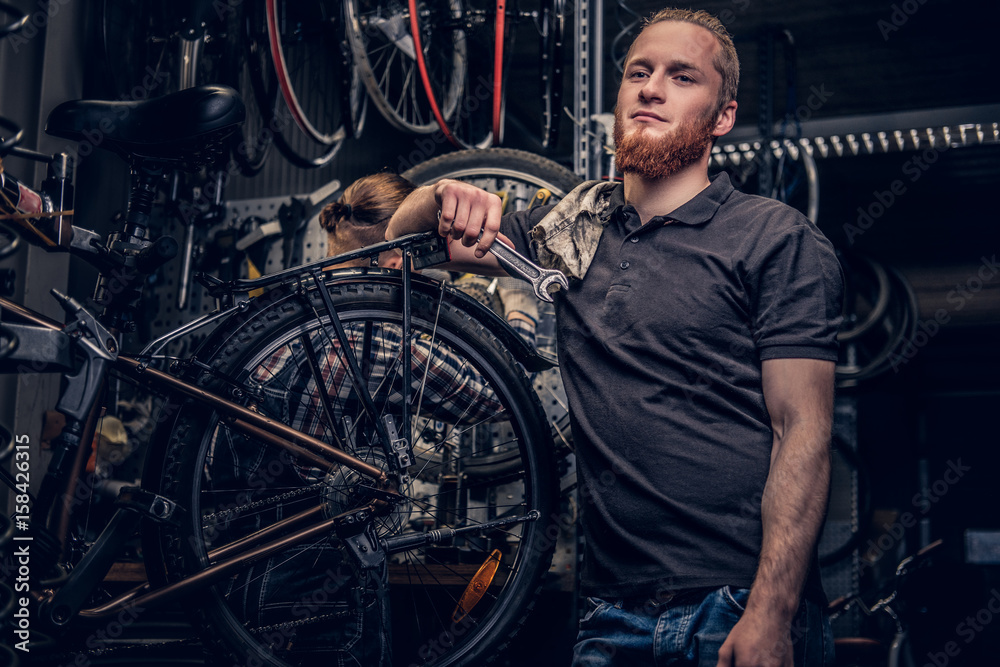 Bicycle mechanic in a workshop with bike parts and wheel on a background.