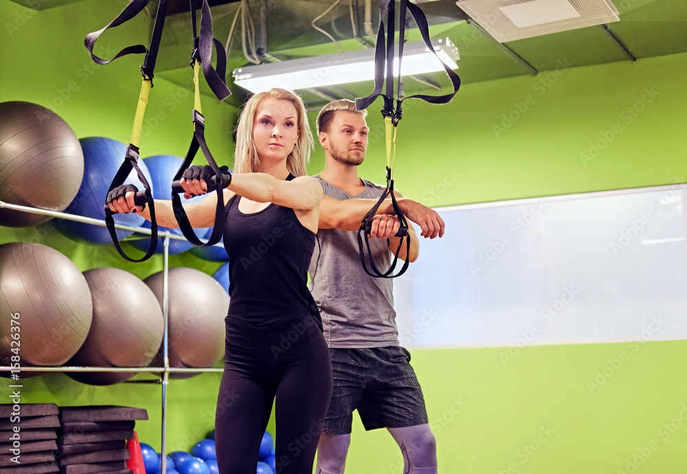 Sporty male and female doing trx straps exercises in a gym club.