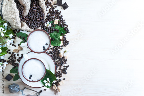 Two cups of freshly brewed  frothy cappuccino. Spilled coffee grains  chocolate and cane sugar. Theme of coffee  cappuccino  mocha chino  america no. Beautiful elegant background with place for text  