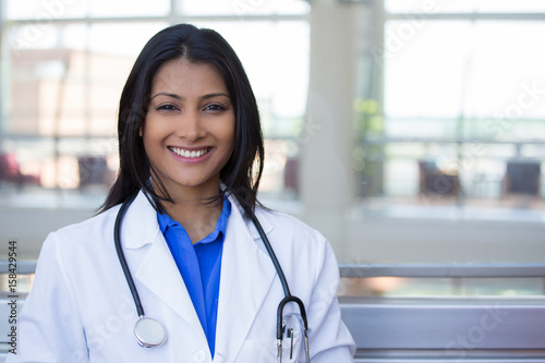 Closeup headshot portrait of friendly, cheerful, smiling confident female, healthcare professional with lab coat. isolated indoor clinic office background. Patient visit.