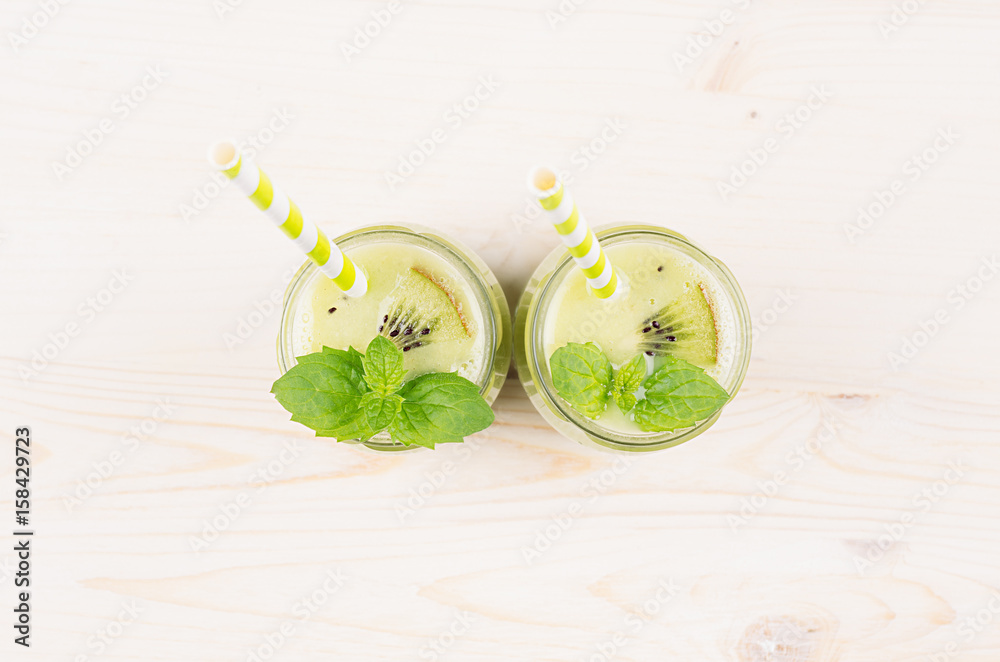 Freshly blended green kiwi fruit smoothie in glass jars with straw, mint leaf, top view. White wooden board background, copy space. Freshly blended green kiwi fruit smoothie in glass jars with straw, mint leaf, top view. White wooden board background, copy space.