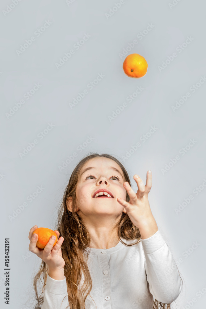 Cute smiling girl juggles with mandarins on a gray background. Isolated Cute smiling girl juggles with mandarins on a gray background. Isolated