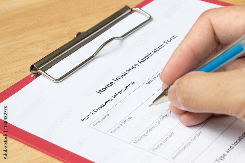 Man fill the home insurance application form with red file on wooden table Man fill the home insurance application form with red file on wooden table