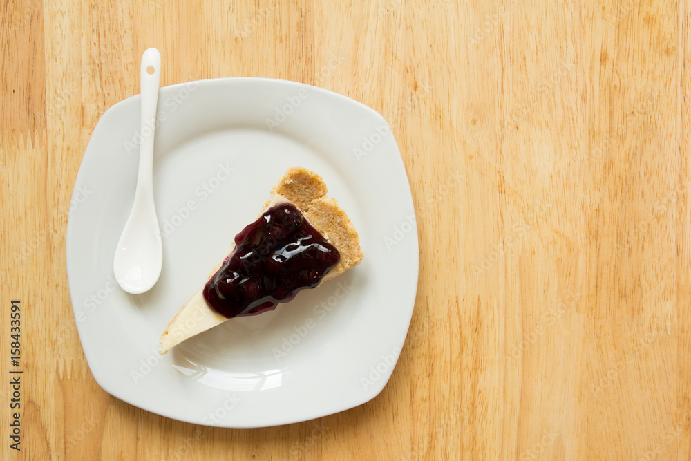 Blueberry cheese cake on white dish with spoon on wooden table background Blueberry cheese cake on white dish with spoon on wooden table background