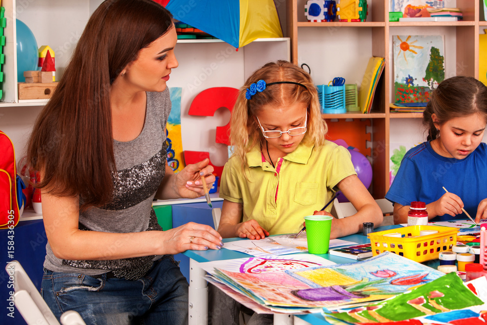 Fototapeta premium Kids playroom organization of children painting and drawing in kid's club. Craft lesson in primary school. Kindergarten teacher and small students work together. Boys at drawing lesson. Girl paints