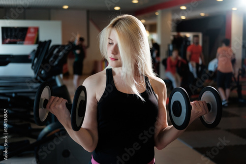 blond girl doing exerсise with Dumbbells in gym
