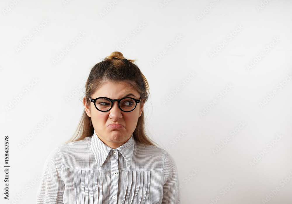 Comic portrait of young offended female in striped shirt and glasses with a raised eyebrow and looking away with angry or irritated expression on her face. Negative womans emotions on her period