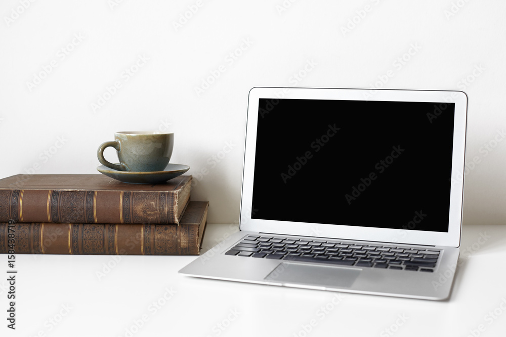 Close up of modern office desktop with blank copy space screen, old books, coffee cup on white wall background. Workplace of a academic historian. History and modern technology concept. Mock up Close up of modern office desktop with blank copy space screen, old books, coffee cup on white wall background. Workplace of a academic historian. History and modern technology concept. Mock up