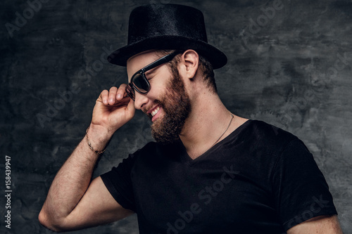 Portrait of bearded male in a black t shirt, cylinder hat and sunglasses.
