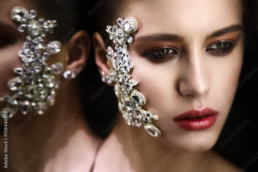 Studio fashion portrait of attractive woman with gemstones on fer face