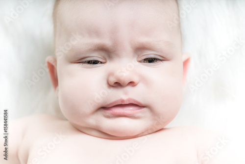 Crying baby lies on a white fluffy background