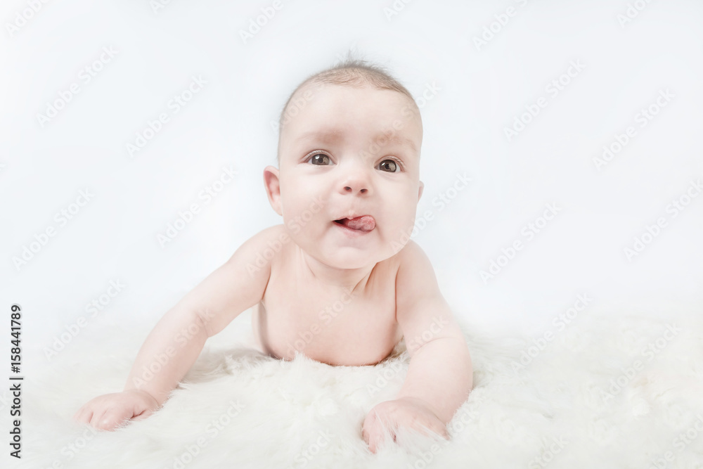 Cute baby lies on a white fluffy background and showing tongue Cute baby lies on a white fluffy background and showing tongue