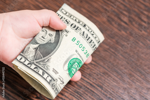 Dollars bundle in the hand of a baby on a wooden background