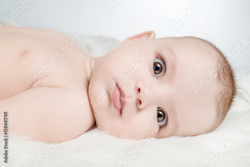 Cute baby lies on a white fluffy background and looking forward