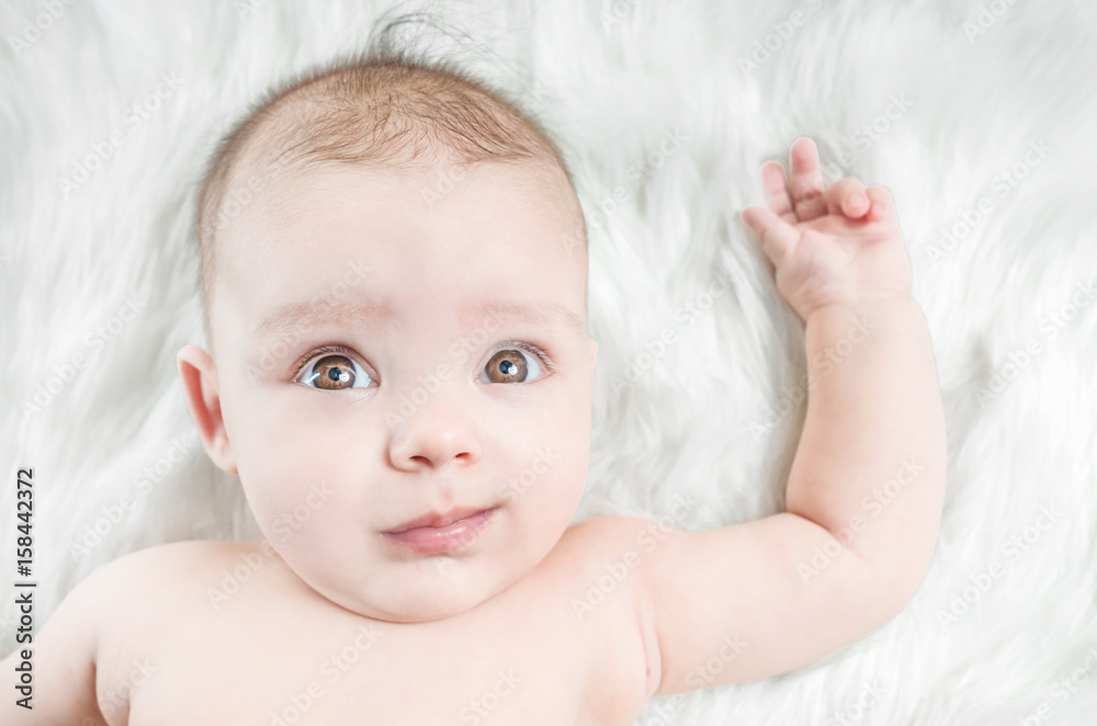 Cute baby lying on a white fur with hand raised Cute baby lying on a white fur with hand raised