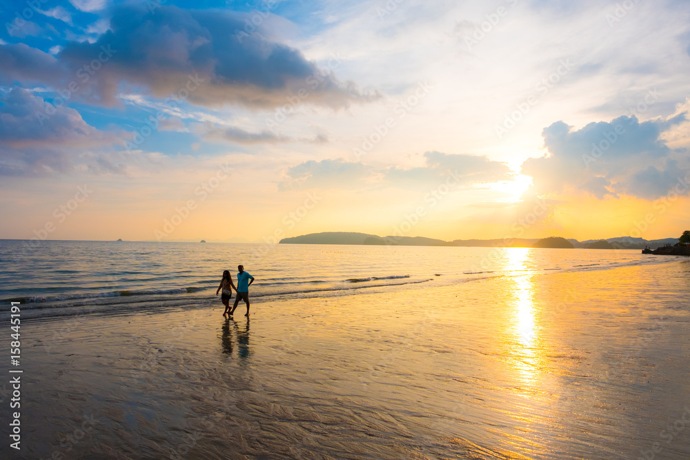 Man and Woman walking on tropical beach with Sunset at Krabi, Thailand
