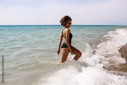 High fashion look.glamor beautiful sexy stylish brunette young female model with bright make-up, with perfect sunbathing clean skin in a black swimsuit on the beach in fashion style