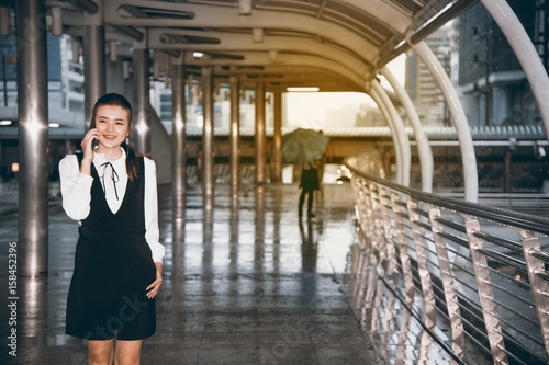 Asian pretty woman use  smartphone at landmark bridge crossing in city in rainy day. © topten22photo