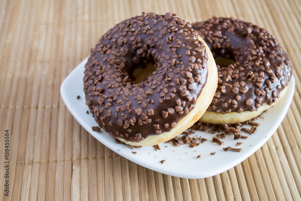 Chocolate donuts in the white plate on the light brown wooden background Chocolate donuts in the white plate on the light brown wooden background