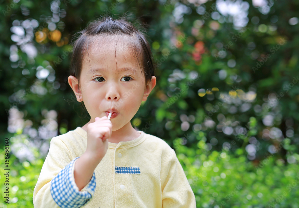 Little child girl enjoy eating lollipop candy in the park.
