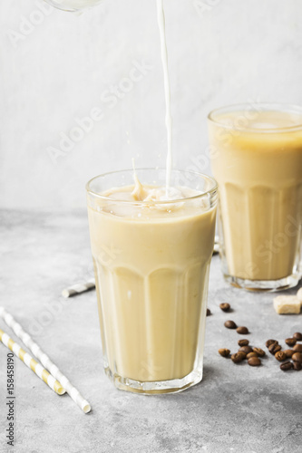 Milk pouring in ice coffee in a tall glass on a gray background