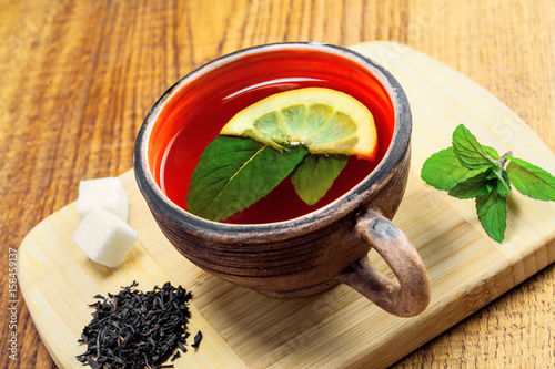 Delicious healthy hot herbal drink made of Ceylon black tea, fresh mint leaves and lemon in a rustic clay mug on a wooden table.