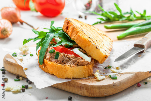 Classic tuna salad sandwich with tomato, onion and arugula on a white table. Delicious healthy meal made of fish, vegetables and toasts.