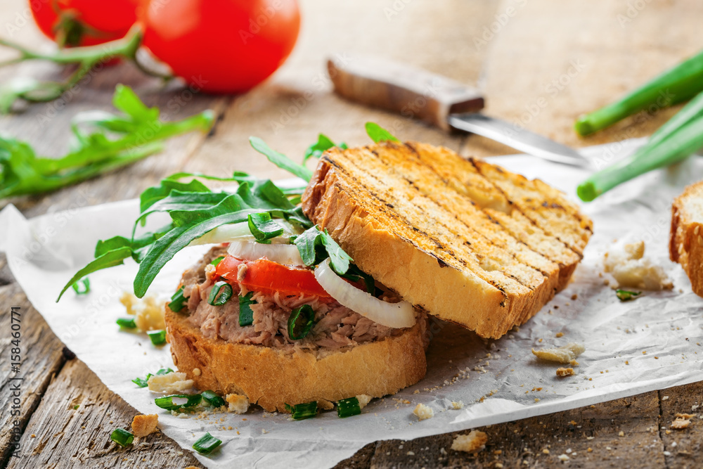 Classic tuna salad sandwich with tomato, onion and arugula on a table. Delicious healthy meal made of fish, vegetables and toasts. Classic tuna salad sandwich with tomato, onion and arugula on a table. Delicious healthy meal made of fish, vegetables and toasts.