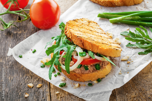 Delicious sandwich made of toasts, tuna, tomato, onion and arugula with ingredients on a table. Traditional healthy food.