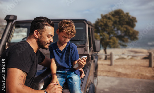 Father and son in front of car using smart phone