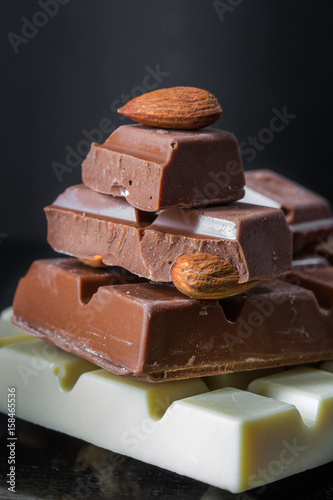Pieces of milk chocolate with almonds and tiles of white chocolate with hazelnuts on a dark old glossy background