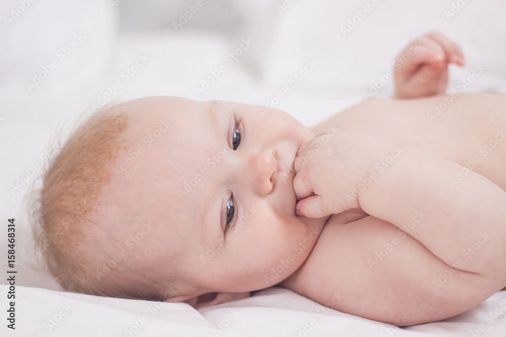 portrait of Cute baby with fingers in mouth in white bed portrait of Cute baby with fingers in mouth in white bed