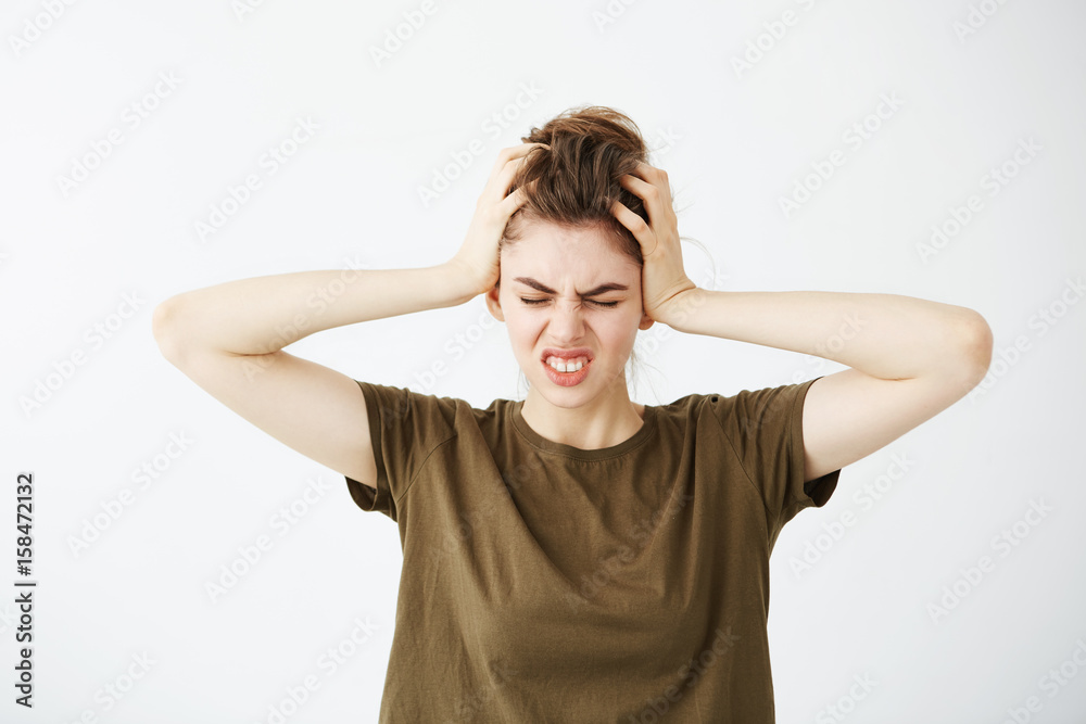 Displeased nervous young girl holding head looking at camera over white background. Headache. Displeased nervous young girl holding head looking at camera over white background. Headache.
