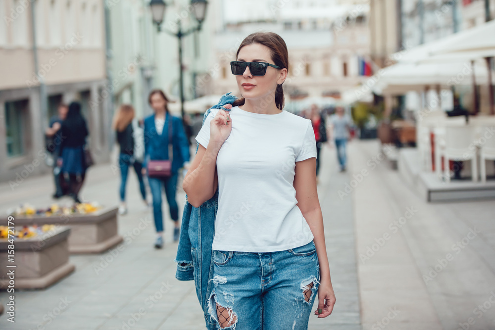 Attractive girl in sunglasses walking along the street. White t-shirt. Mock-up.