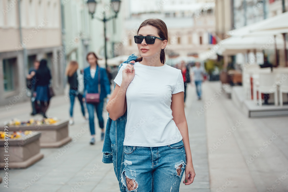 Fototapeta premium Attractive girl in sunglasses walking along the street. White t-shirt. Mock-up.