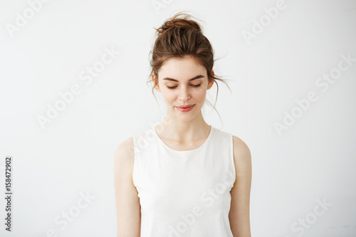 Portrait of young beautiful brunette girl smiling looking down over white background.
