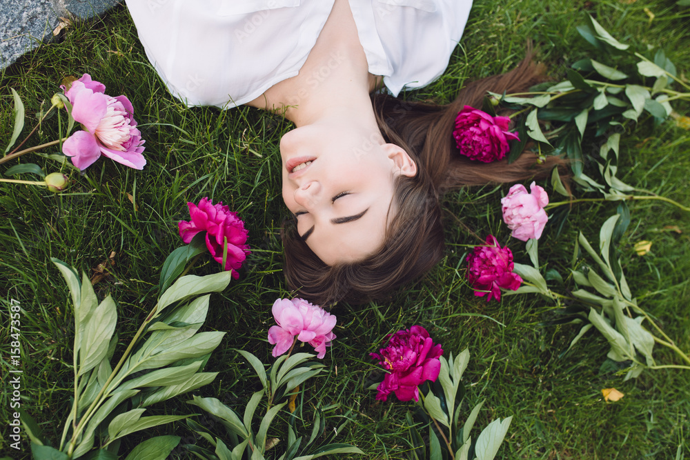 Woman lying on grass with flowers peonies around