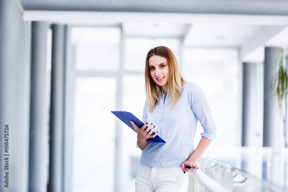 Beautiful business woman standing and looking straight while holding paper board Beautiful business woman standing and looking straight while holding paper board