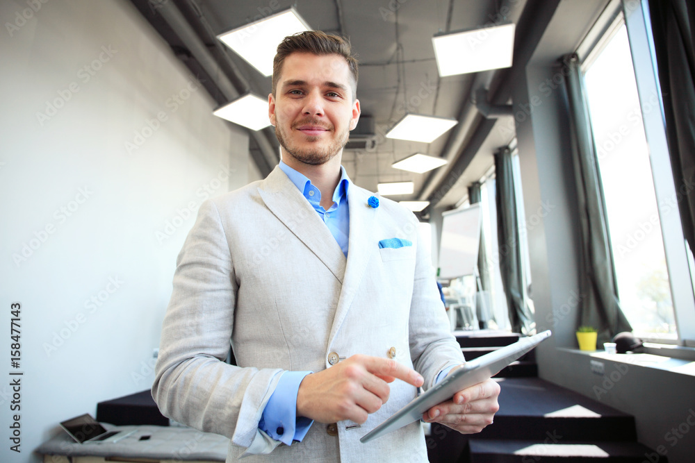 Fototapeta premium Working on new tablet. Low angle view of confident young man working on digital tablet while standing in front of the big window in office or cafe