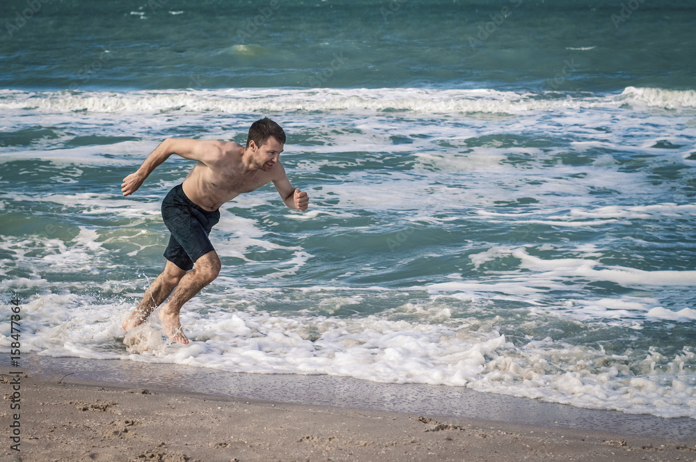 Fototapeta premium The guy is running at the beach close to the water