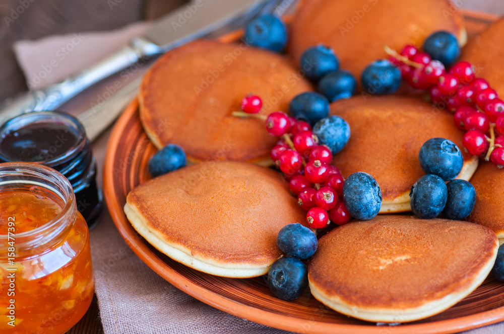 Close up of fluffy pancakes with fresh berries, blueberry and orange jam served on a white plate. Healthy breakfast concept.