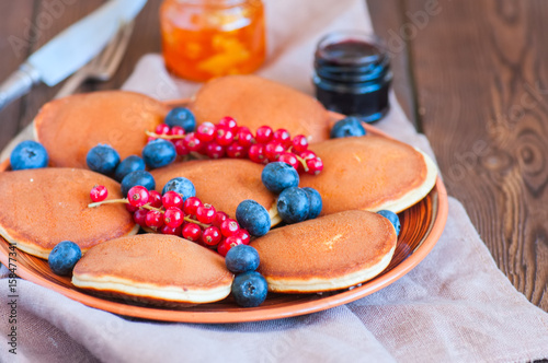 Fototapeta Naklejka Na Ścianę i Meble -  Close up of fluffy pancakes with fresh berries, blueberry and orange jam served on a white plate. Healthy breakfast concept.