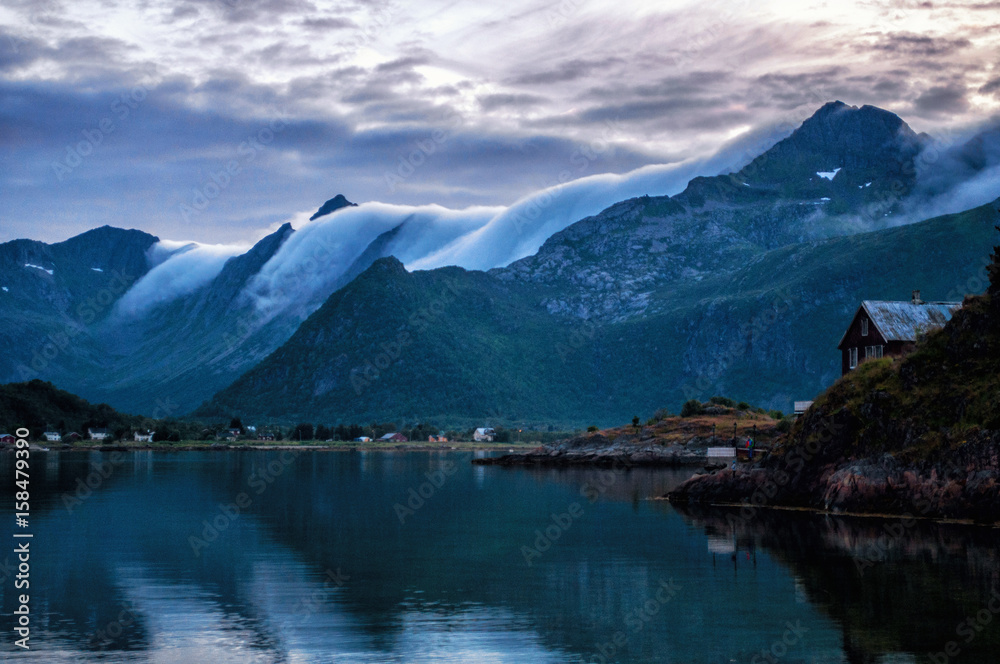 Sunset and clouds moving over the rocky mountains above the sea. Lofoten, Norway.