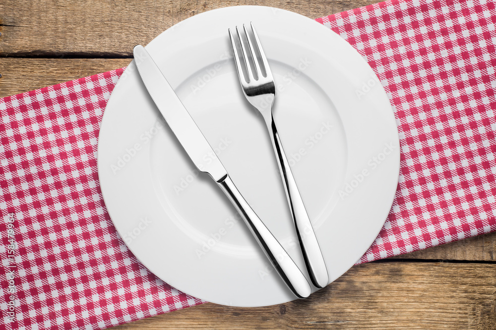 empty plate on a wooden background, a napkin in a red and white cage, a fork a knife empty plate on a wooden background, a napkin in a red and white cage, a fork a knife